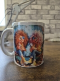 Eine weiße Keramiktasse steht auf einer Holzoberfläche vor einer Wand mit Backsteinmuster. Auf der Tasse befindet sich ein farbenfrohes Illustrationsmotiv sowie der gut lesbare Schriftzug „Ich wünschte Du wärst hier!“ in schwarzer Schrift. Rechts im Hinte